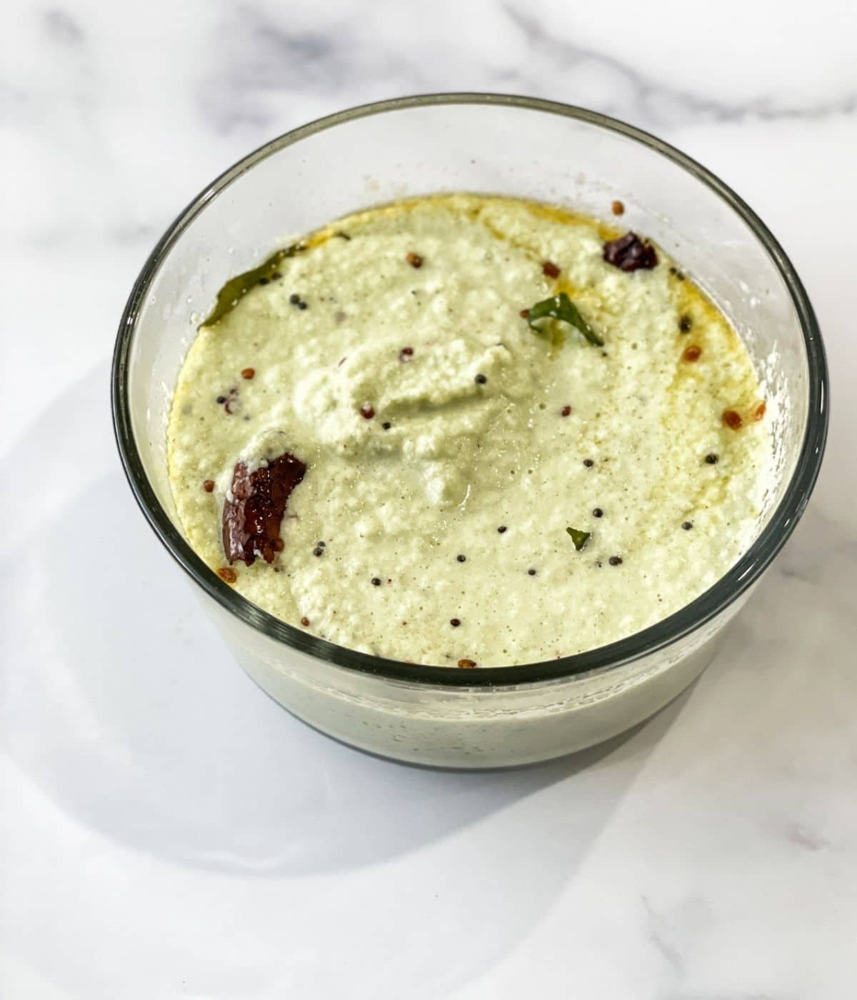 A glass container is filled with coconut chutney.