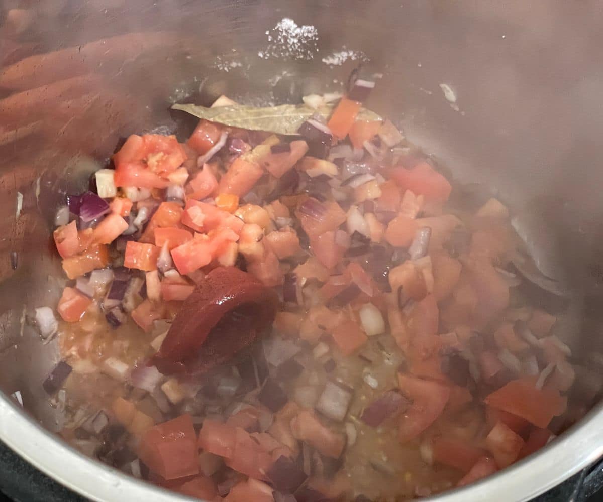 A pot has tomatoes, onion and spices for aloo matar curry.