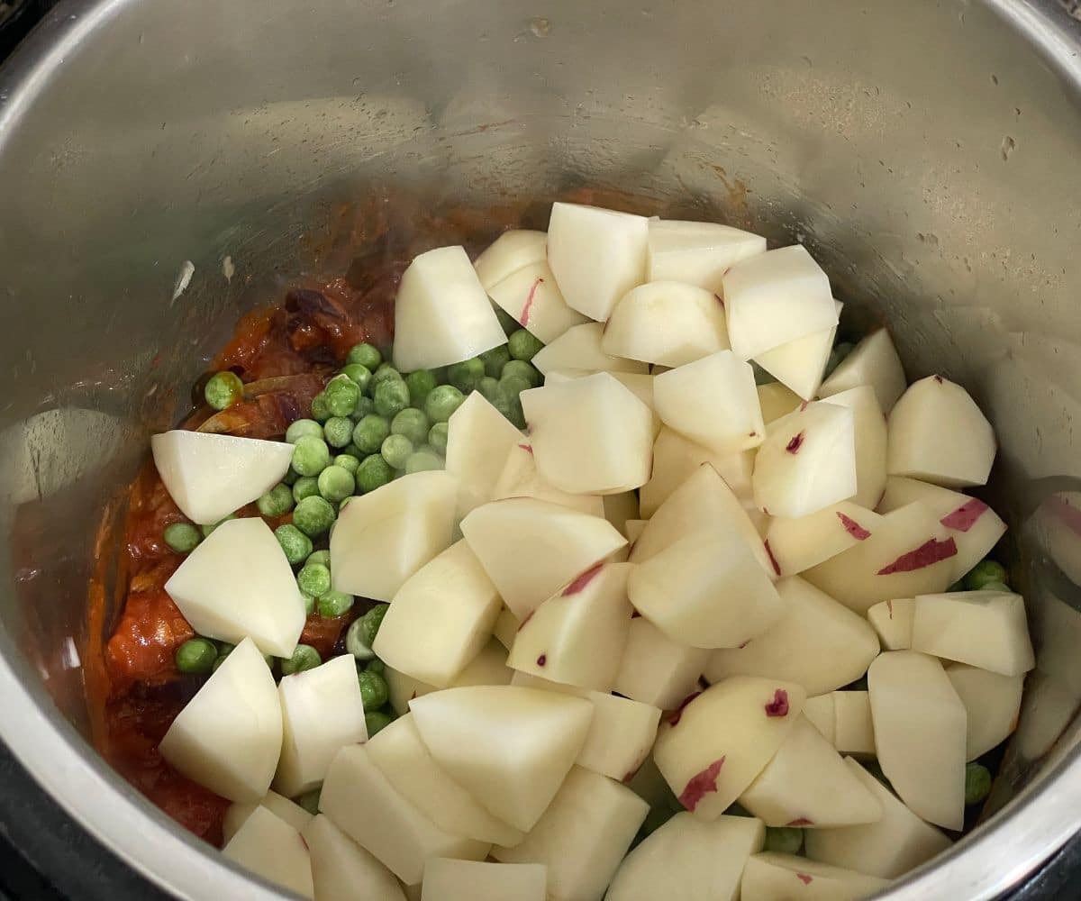 An instant pot is filled with aloo matar curry ingredients.