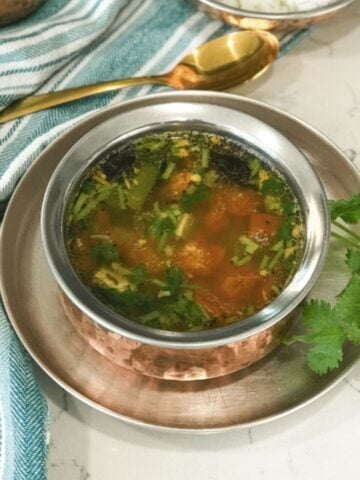 A copper bowl is with tomato rasam without rasam powder.