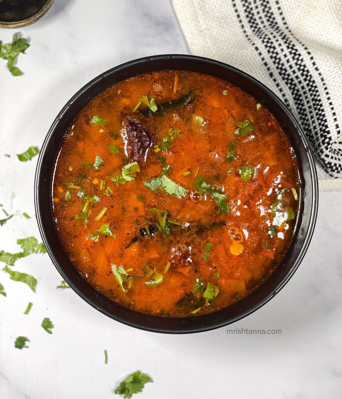 A bowl of tomato rasam is on the table.