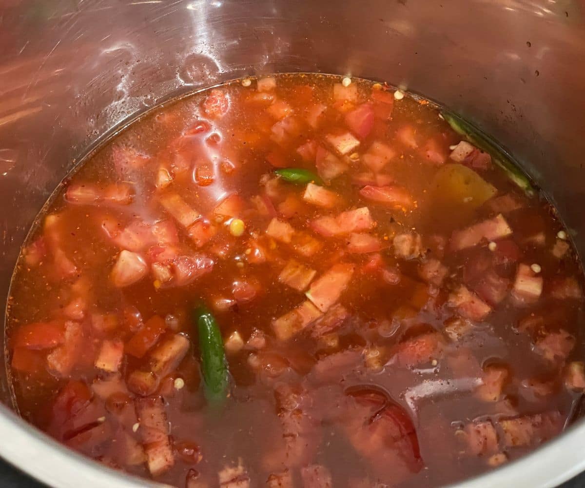 An instant pot has tamoto rasam ingredients and water.