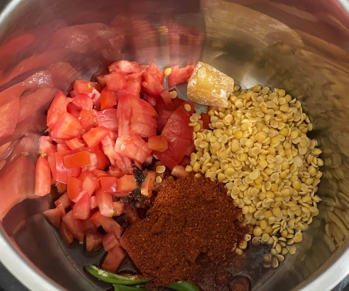 An instant pot is filled with all the tamato rasam ingredients.