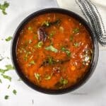 A bowl of Tomato rasam is on the table.