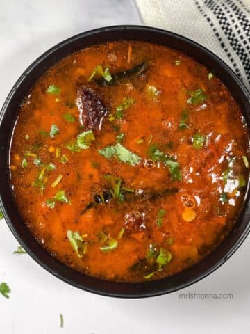 A bowl of Tomato rasam is on the table.