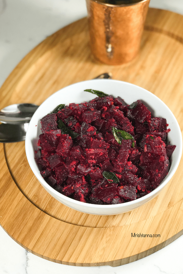 A bowl of beetroot palya placed on a wooden surface with spoons