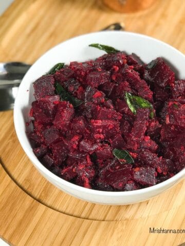 A bowl of beetroot poriyal is on the table along with two spoons