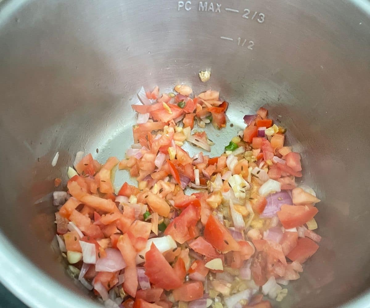 An Instant pot is with tomatoes and onions for curry