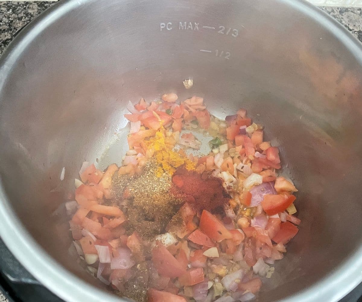 A pot is filled with spices and tomatoes with heat on