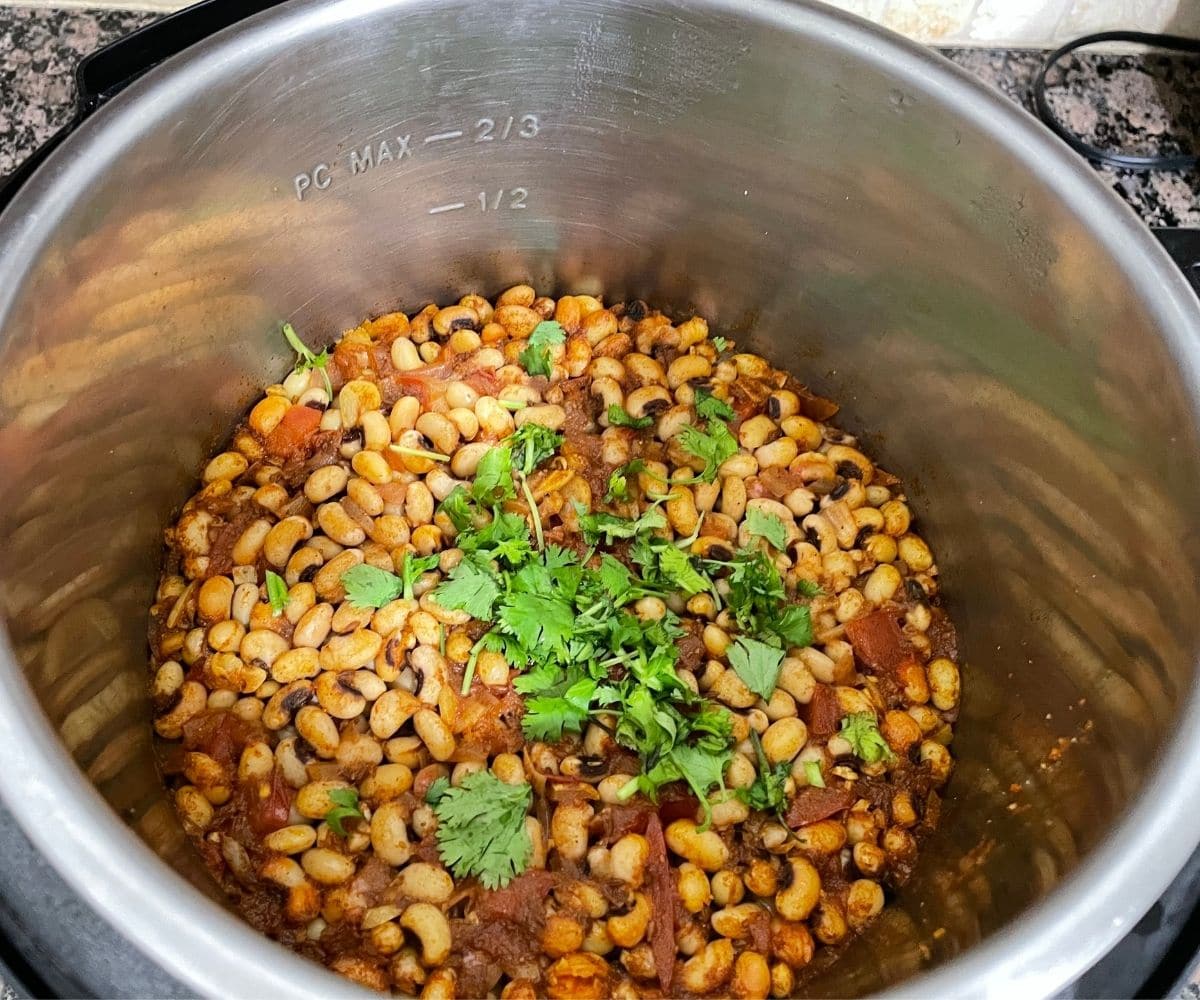 An Instant pot is filled with black eyed peas curry and topped with chopped cilantro 