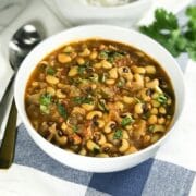 A white bowl is with black eyed peas curry along with spoons on the table