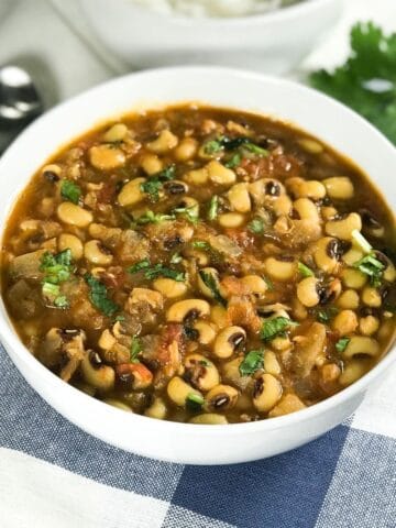 A white bowl is with black eyed peas curry along with spoons on the table