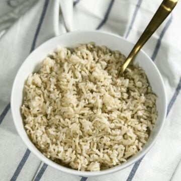 A bowl of instant pot brown rice is on the table with spoon inserted.