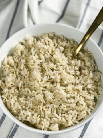 A bowl of instant pot brown rice is on the table with spoon inserted.