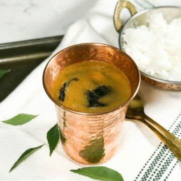 A copper tumbler is filled with horse gram rasam on the table.