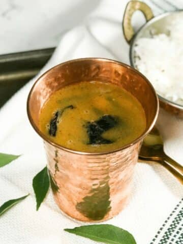 A copper tumbler is filled with horse gram rasam on the table.
