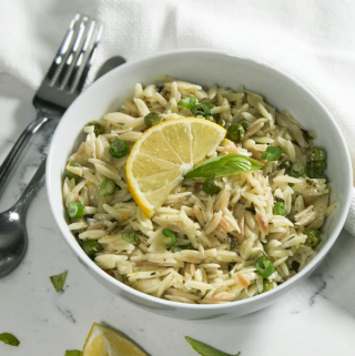 A white bowl full lemon orzo with a side of the lemon wedge for garnish