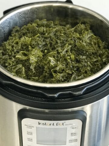 An instant pot is with cooked kale.