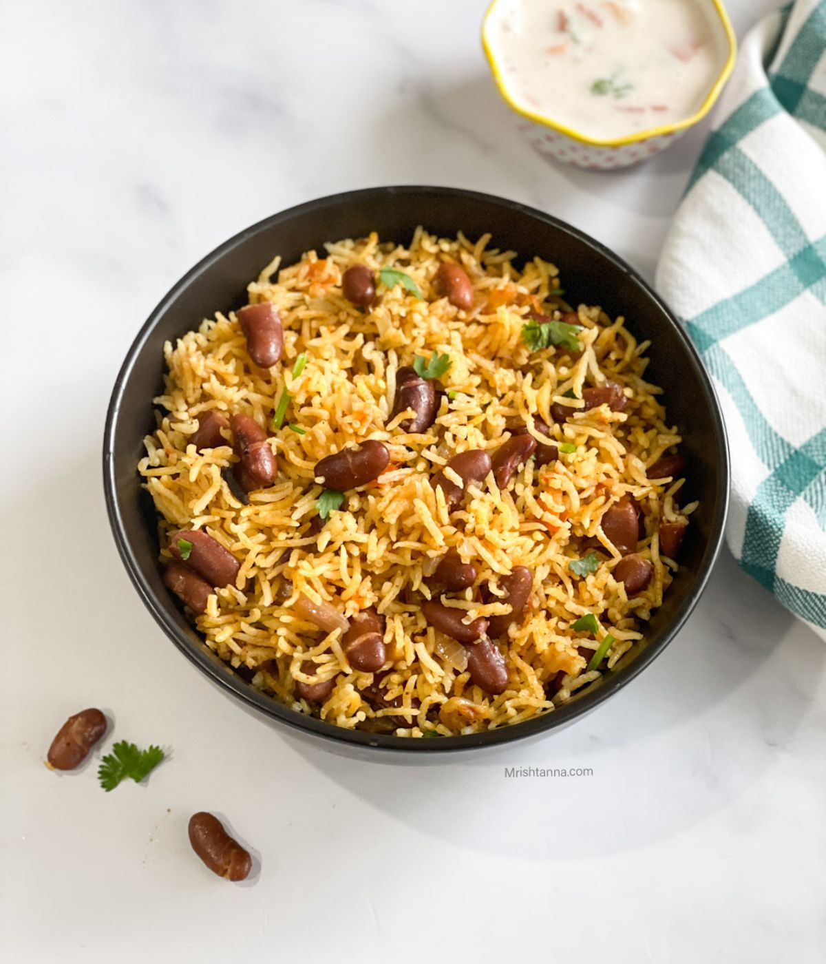 A bowl of rajma pulao is on the table with a bowl of raita.
