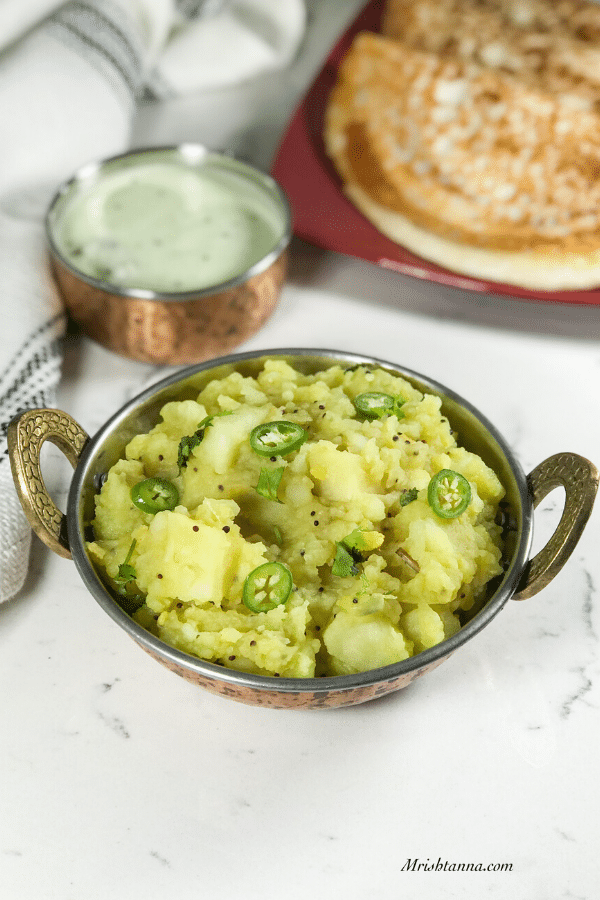 A bowl of potato masala is on the table along with dosa