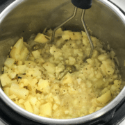 An instant pot is filled with potato masala and masher is inserted