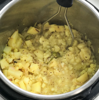 An instant pot is filled with potato masala and masher is inserted