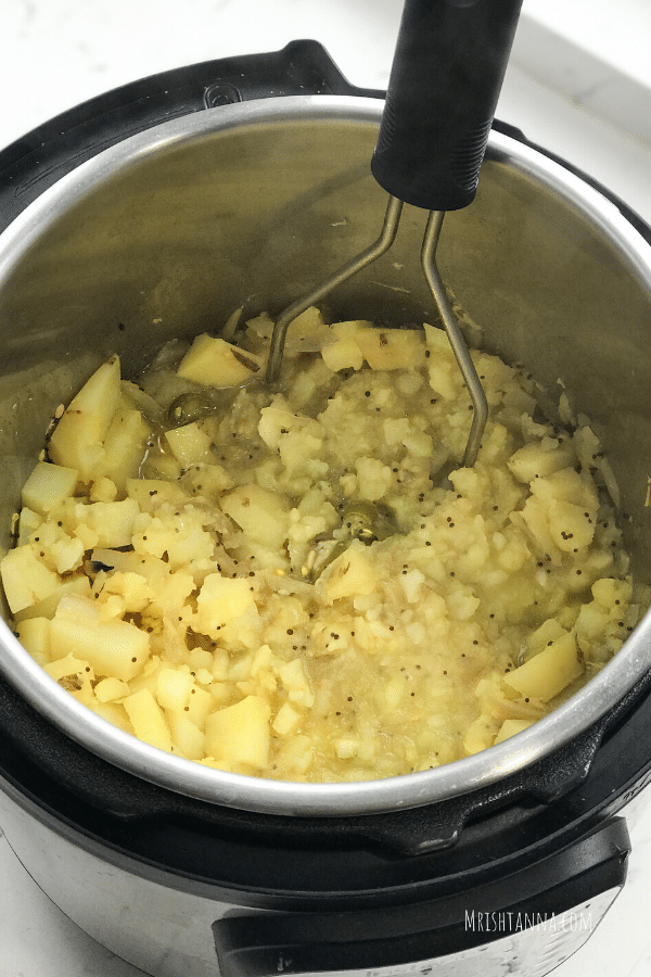 An instant pot is filled with potato masala and masher is inserted