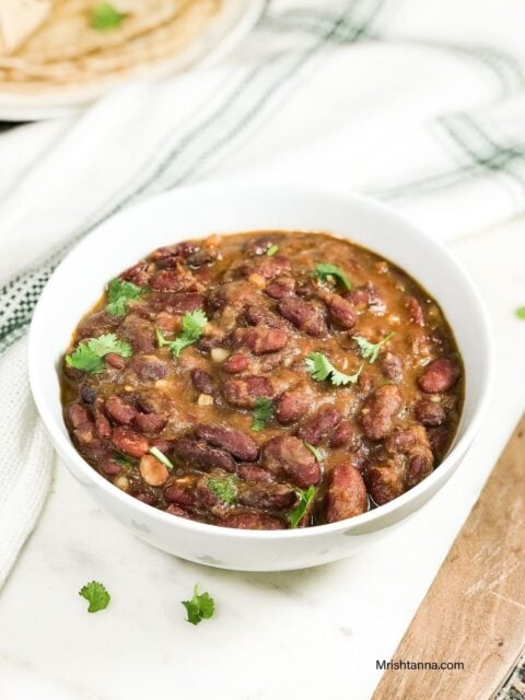 A white bowl of rajma and topped with cilantro is on the serving tray