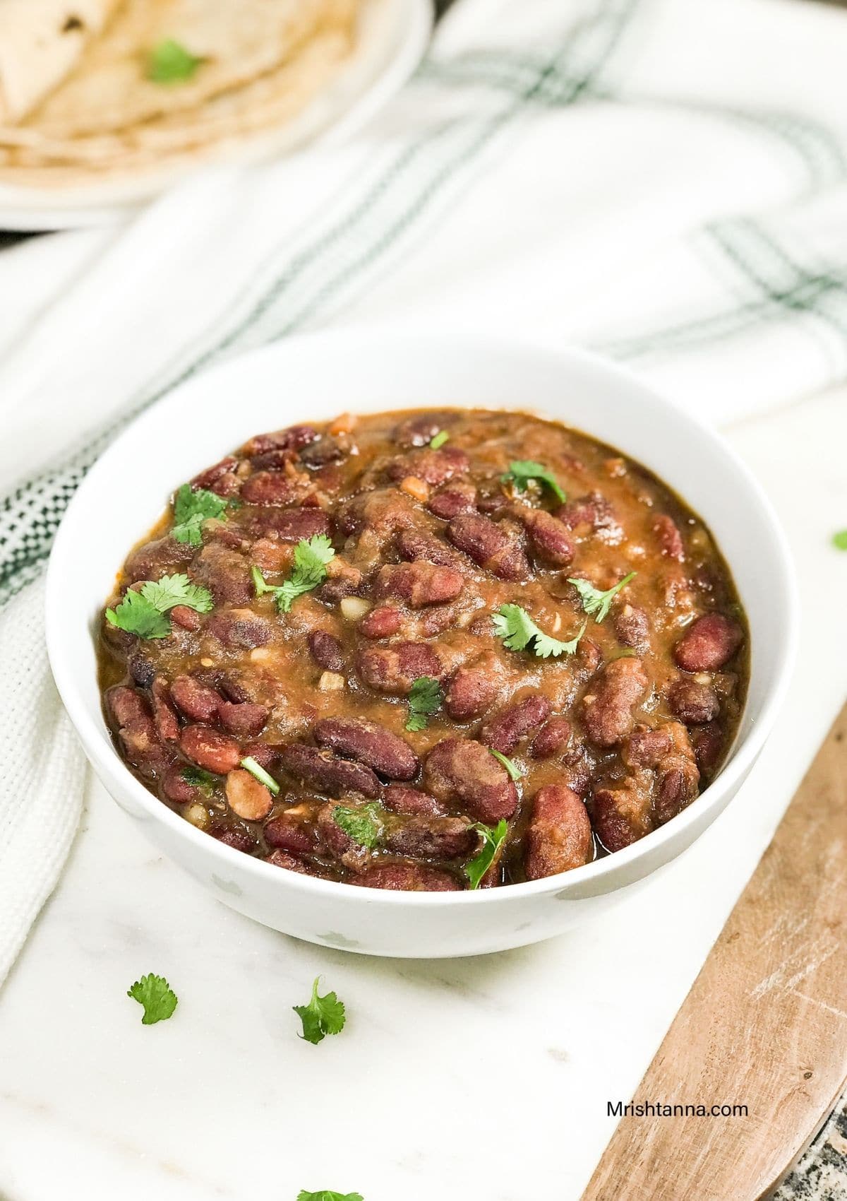 A white bowl of rajma and topped with cilantro is on the serving tray