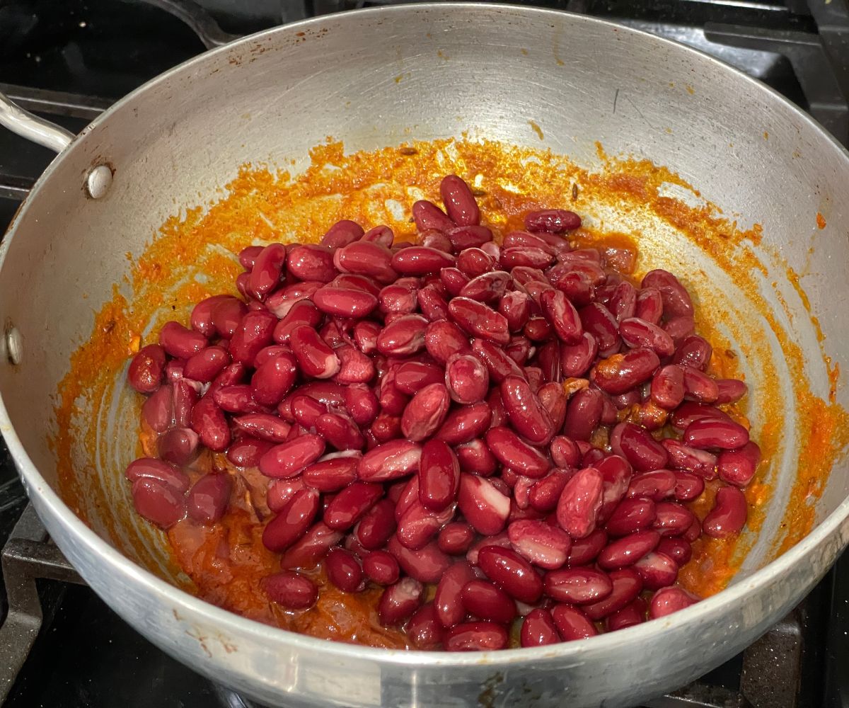 A pot is with masala and canned kidney beans over the heat.