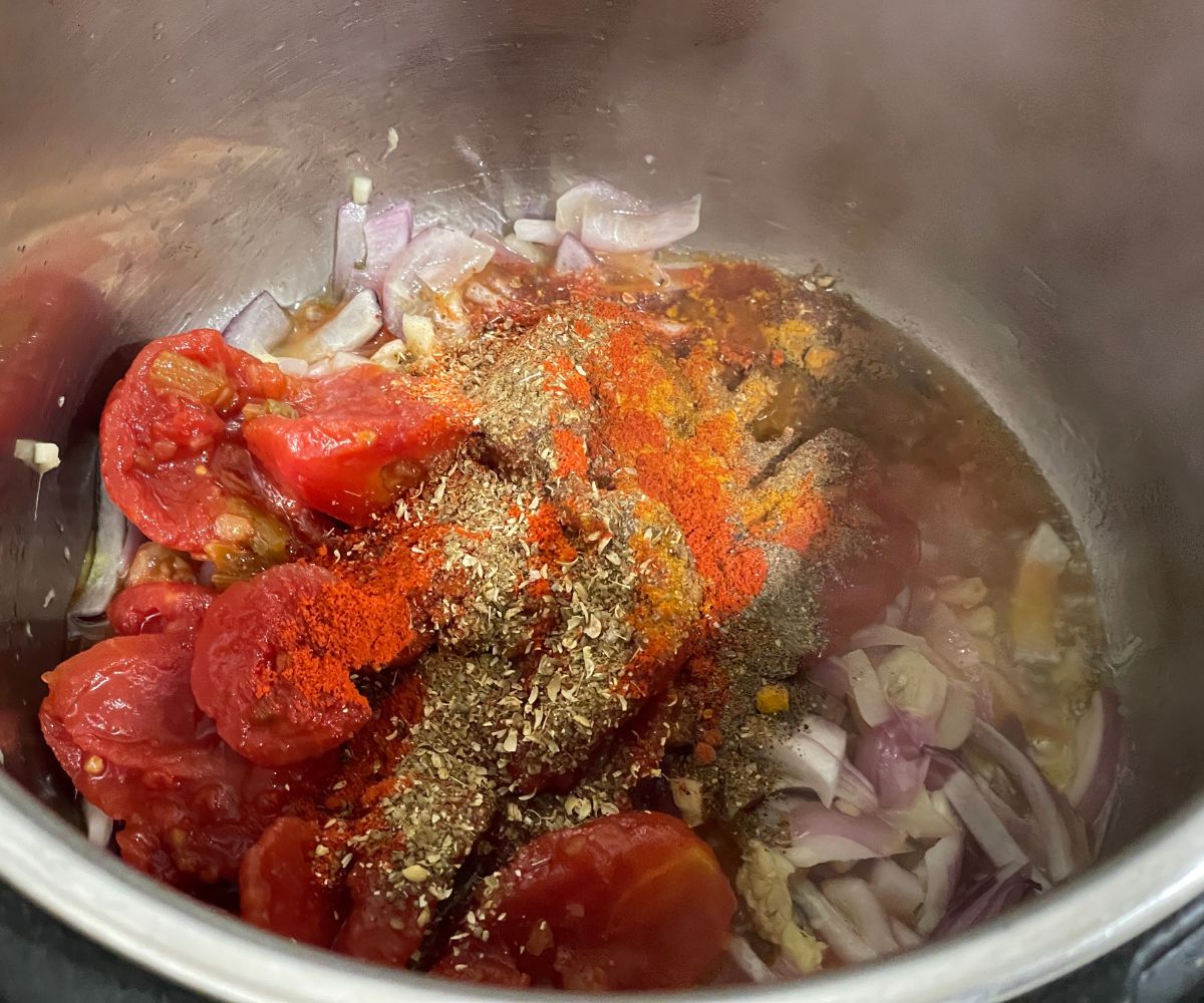 An instant pot has spices and canned tomatoes.