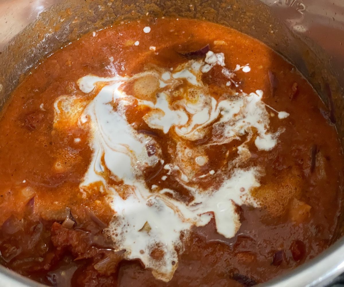 An instant pot has tomato sauce and all the ingredients for tikka masala pasta.