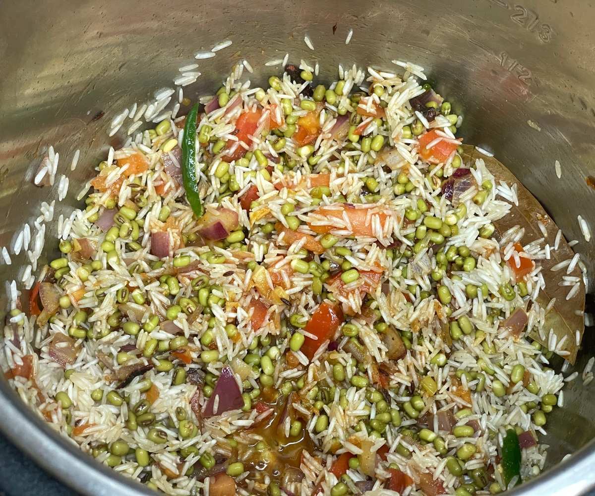 An instant pot is with rice, green gram and spices for pulao recipe.