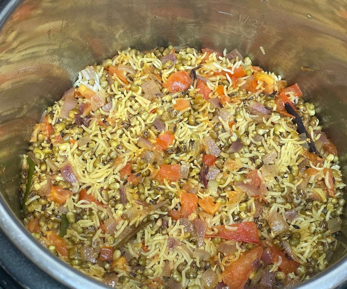 An instant pot is with cooked green moong pulao rice.