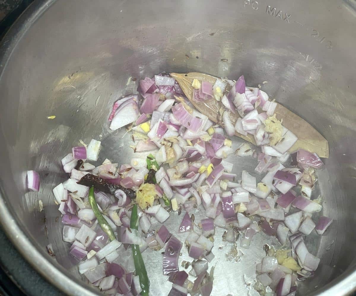 An instant pot has onion, ginger and cumin for green moong rice.
