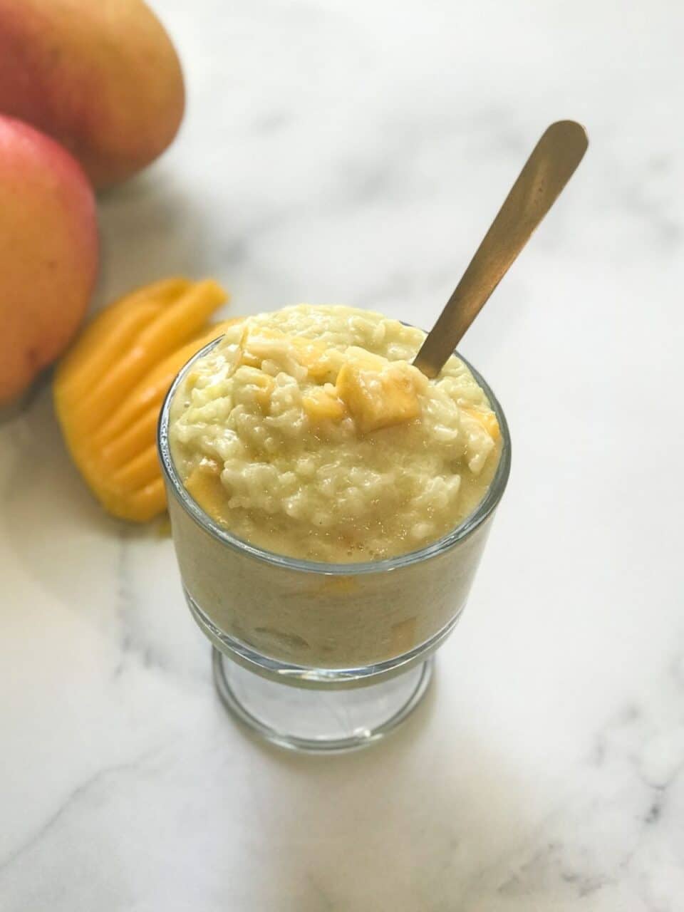 A bowl of mango rice pudding is on the flat surface along with chopped mangoes