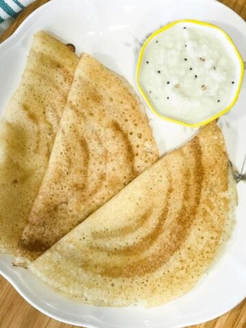 A plate is with aval dosa and coconut chutney.