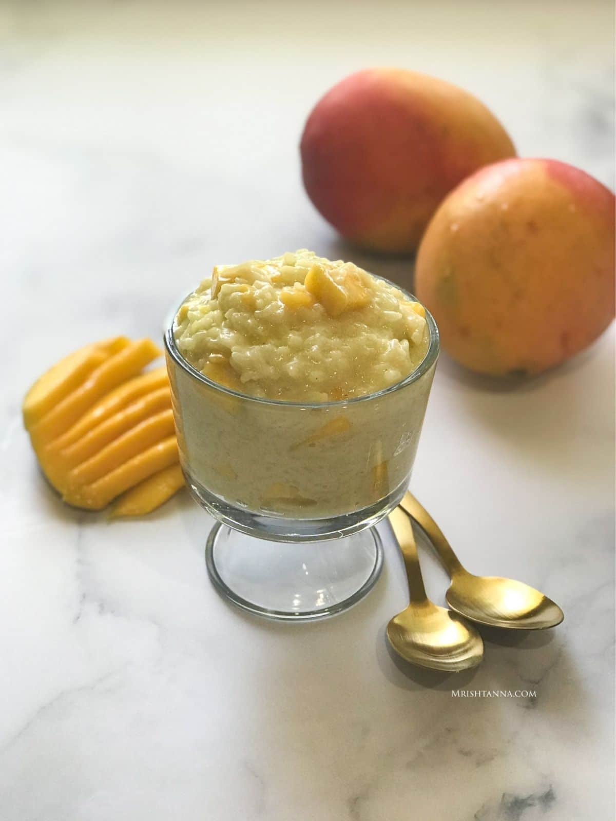 A glass bowl of rice pudding is on the table with mangoes