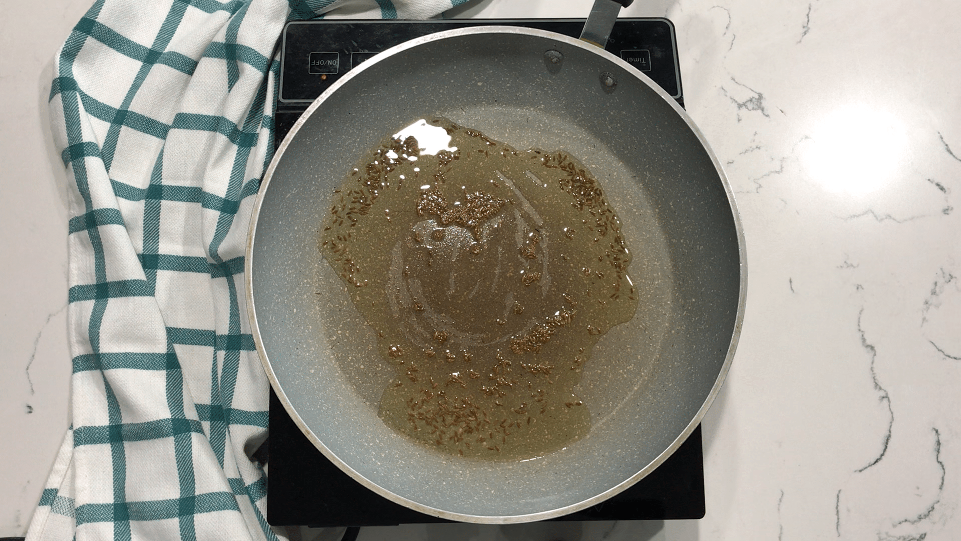 A pan on a stove top with oil and cumin