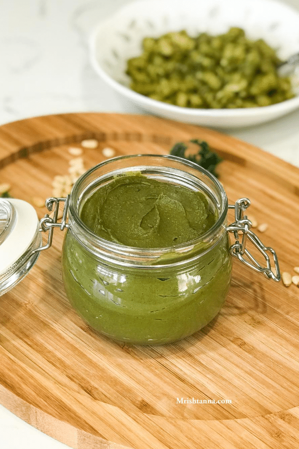 A jar of sauce sitting on top of a wooden table, with Kale and Pesto