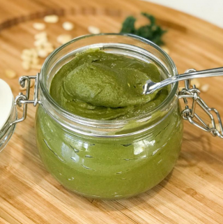 A jar of sauce sitting on top of a wooden table, with Pesto