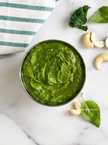 A bowl of kale cashew pesto is on the surface.