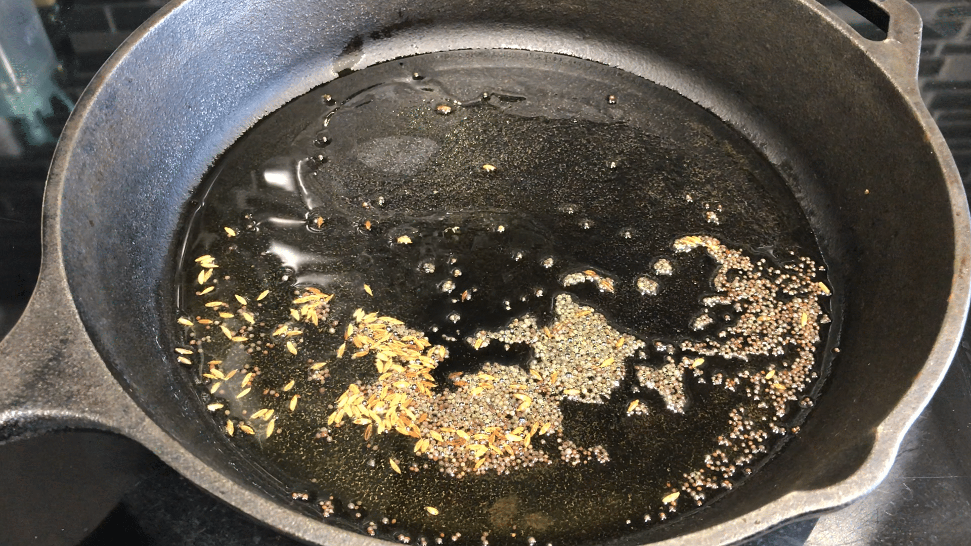 A close up of a cast iron pan on a stove, with oil and spices