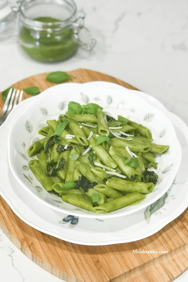 A plate of food on a table, with basil and pesto pasta