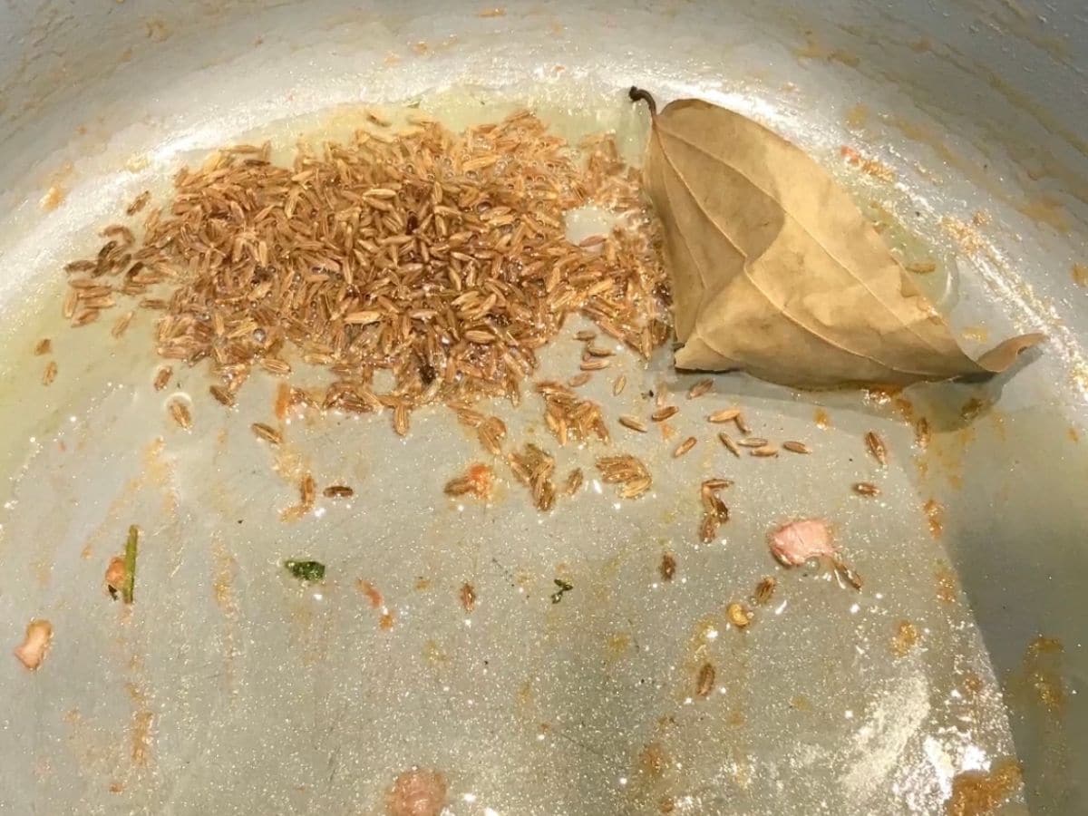 A medium size pan is with oil, cumin seeds and bay leaf over the stove top.