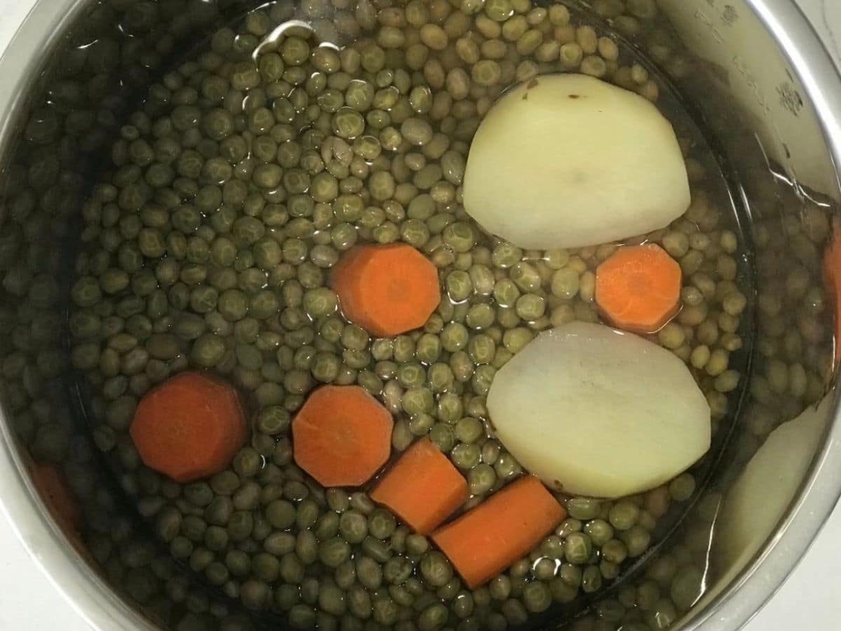 An instant pot is with peas,carrots and potatoes