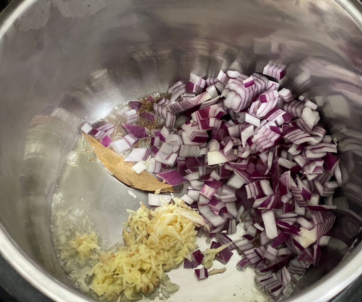 An instant pot is with onions and ginger garlic.