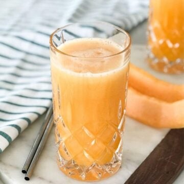 A glass of cantaloupe juice next to a cantaloupe spear