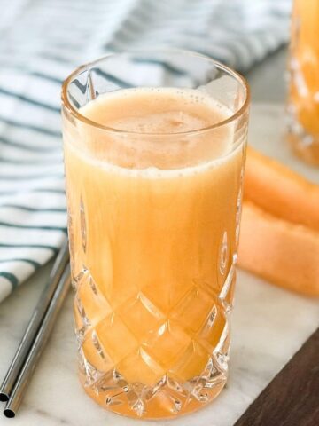 A glass of cantaloupe juice next to a cantaloupe spear