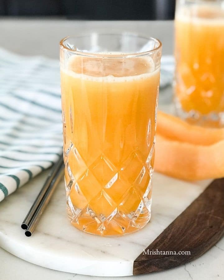 A glass of cantaloupe juice next to a cantaloupe spear